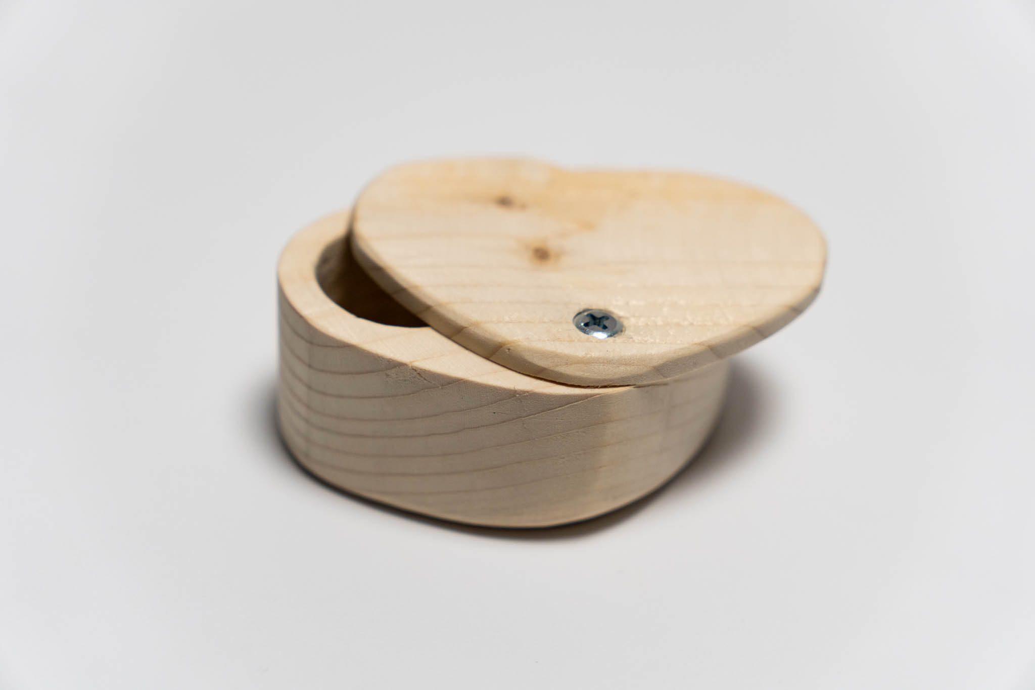 a small heart-shaped wooden beige box with its lid ancored around the tip, slightly open